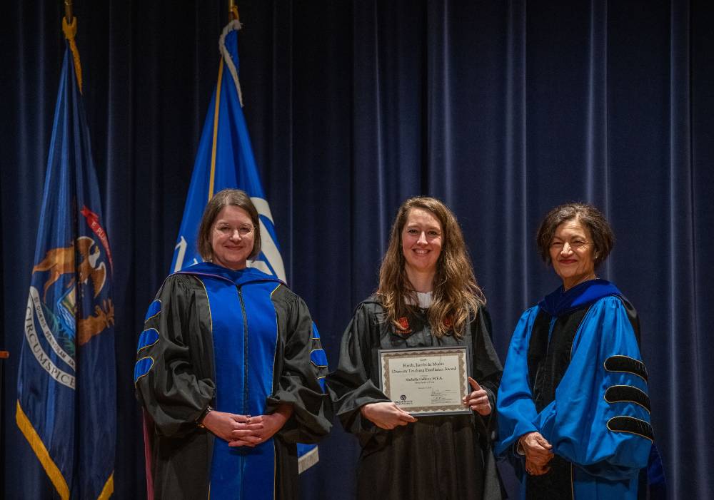 Provost Mili smiles for picture with 2 women on stage